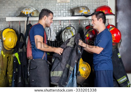 Happy firefighters looking at each other while holding jacket in fire station