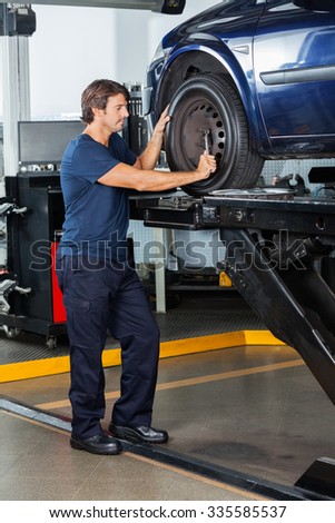 Male mechanic fixing lifted car tire at auto repair shop