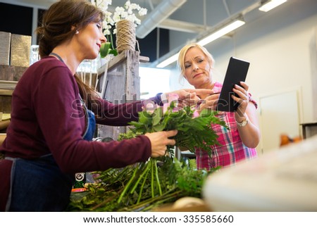 Female customer showing something on digital tablet to florist in flower shop