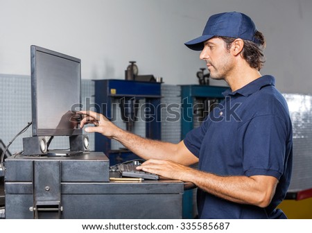 Side view of male mechanic using computer in auto repair shop