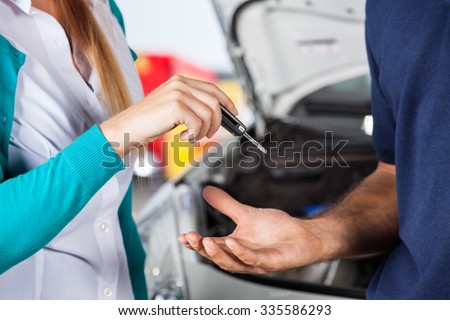 Midsection of female customer giving car keys to mechanic in auto repair shop