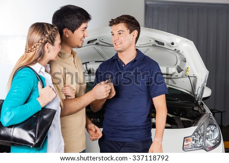 Smiling technician taking keys from couple while standing in front of car at auto repair shop