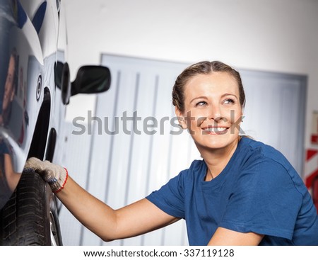 Happy female mechanic looking away while fixing car tire at auto repair shop