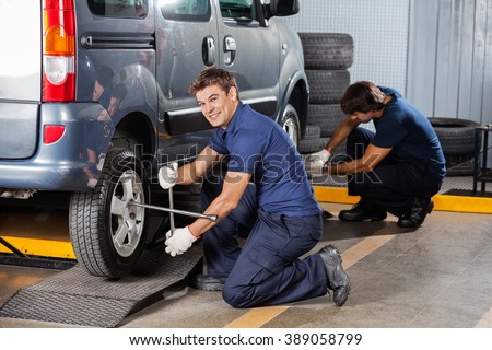 Happy Mechanic Fixing Car Tire At Repair Shop
