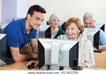 Tutor Assisting Senior Woman During Computer Class