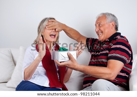 Senior man covering his wife\'s eyes to surprise her with a gift