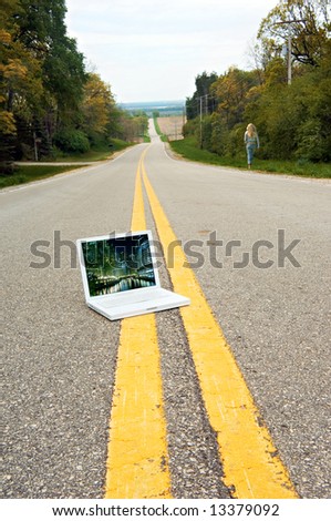 Laptop Computer sitting in the middle of a country road. My photograph is on the screen. Woman is walking away.