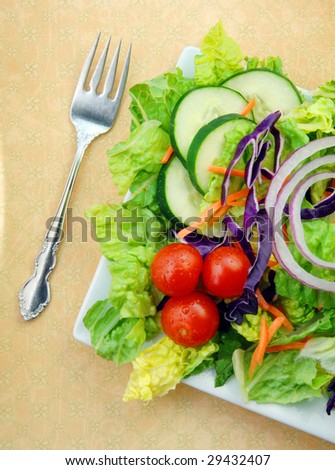 Fresh garden salad with tomatoes, lettuce, cucumbers and onions on a square white plate with a fork.