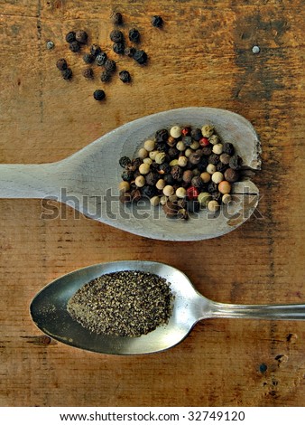 Ground black pepper and peppercorns in spoons on a rustic wood table.