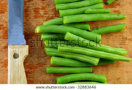 Fresh cut green beans and a knife on a rustic wooden table.