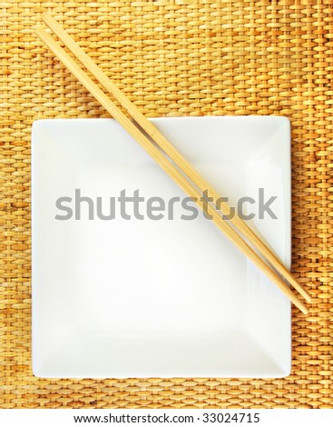 Empty White dish and wooden chopsticks on a bamboo mat.
