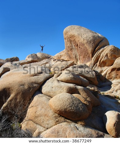 A man standing up on top of a rocky hill out in the desert. Arms up in praise or joy.