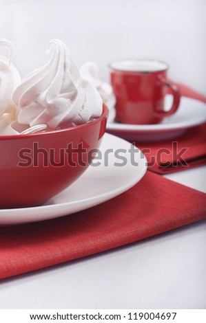 Closeup side view of a red bowl with meringues and away the red cup on the red rag towels.
