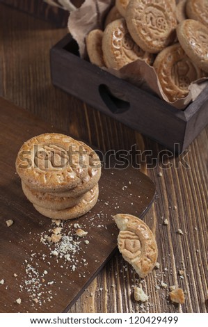 Top view of cookies in the box on wooden board. Biscuits stack and one broken cookie with crumbs on cutting board.
