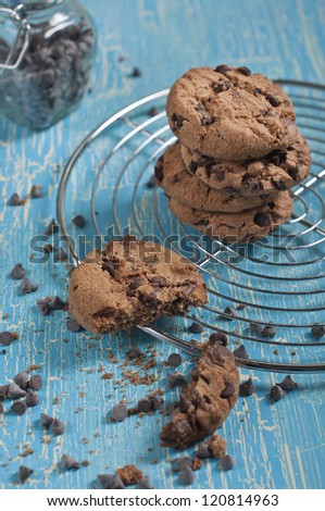 Top closeup view of broken cookie and biscuits with chocolate drops on round iron stand, jars with chocolate drops on cracked blue background