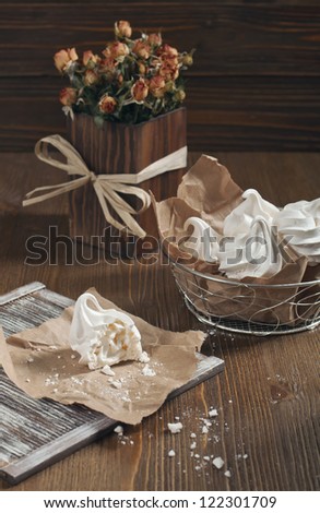 Top view of white broken meringue, metal vase with meringue and dry orange roses in a wooden square vase