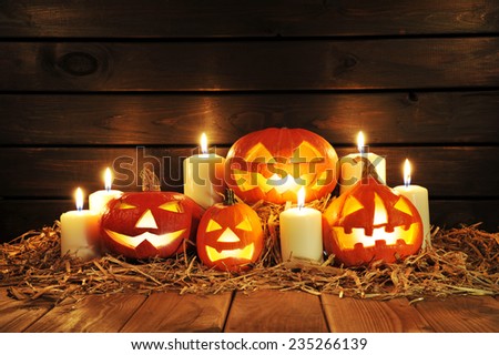four illuminated halloween pumpkins with candles on straw in front of old weathered wooden board in candlelight