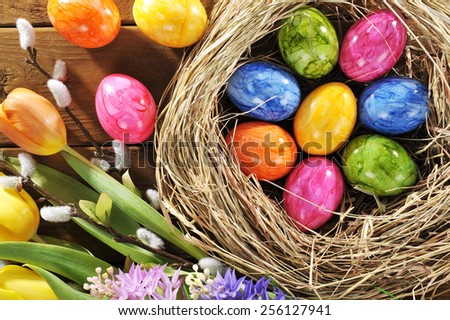 Easter nest with many colored henÃ¢Â?Â?s eggs, tulip, hyacinth and pussy willow on old wooden board