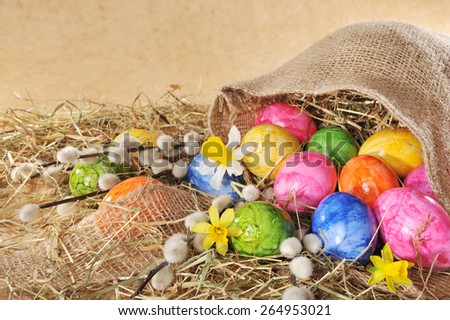 Easter eggs in jute bag with narcissus and catkin on wooden board