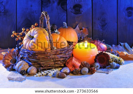 Thanksgiving - different pumpkins, nuts, maize cob and apple in rattan basket with candlelight in blue sunset light