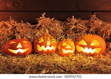 four illuminated halloween pumpkins and straw in front of old weathered wooden board in red light