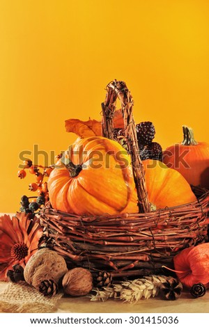Thanksgiving - different pumpkins in rattan basket in front of orange background in candle light