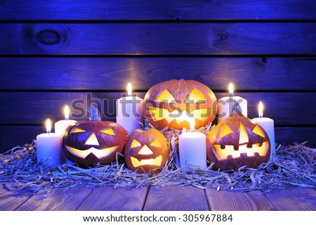 four illuminated halloween pumpkins with candles on straw in front of old weathered wooden board in blue sunset light
