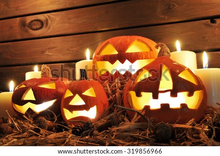 four illuminated halloween pumpkins on straw in front of old weathered wooden board in candlelight
