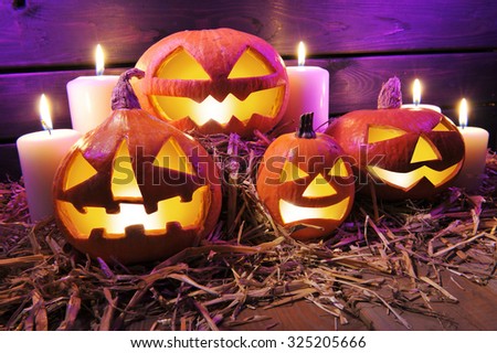 four illuminated halloween pumpkins on straw in front of old weathered wooden board in crazy violet halloween light