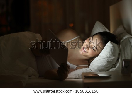 Happy woman watching tv or media content in a tablet on the bed in the night