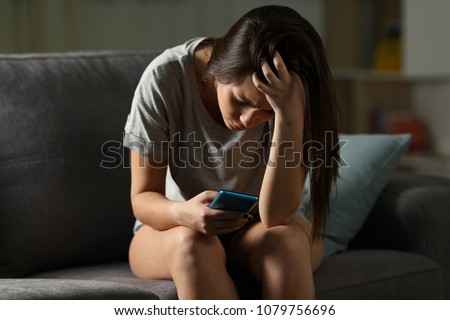 Sad teen being victim of cyber bullying online sitting on a couch in the living room at home