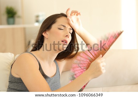 Woman suffering a heat wave using a fan sitting on a couch in the living room at home