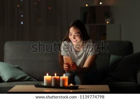 Woman using a smart phone in the night with candle lights sitting on a couch in the living room at home