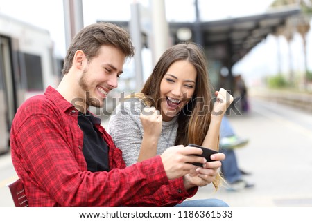 Happy couple winning online games together waiting in a train station