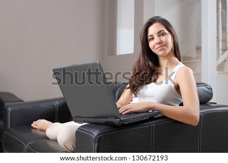 Beautiful woman at home sitting on a couch with a laptop and looking at camera