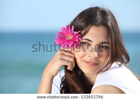 Portrait of a beautiful woman on the beach with a pink flower with the sea in the background