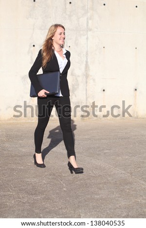 Happy businesswoman walking on the street carrying laptop