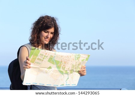 Beautiful tourist woman watching a city map with the sea and the sky in the background