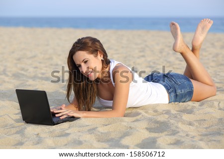 Beautiful teenager girl browsing her netbook computer lying on the sand of the beach with the horizon in the background