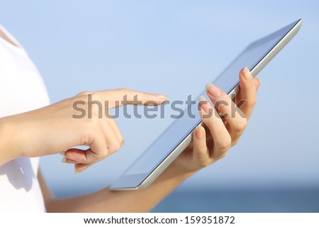 Profile of a woman hands holding and browsing a digital tablet on the beach with the sky in the background
