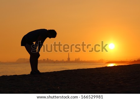 Silhouette Of An Tired Sportsman At Sunset With A City In The Background