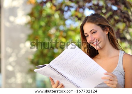 Beautiful teenager girl studying reading a notebook outdoor with a green background