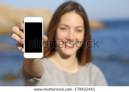 Happy woman showing a smart phone display on the beach with the sea in the background