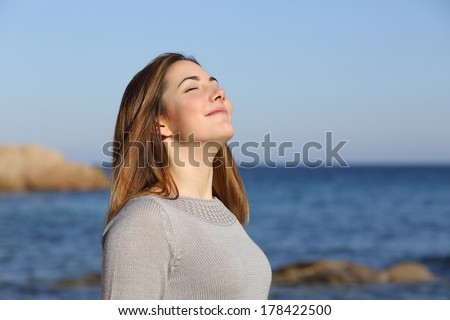 Happy relaxed woman breathing deep fresh air on the beach with the horizon in the background