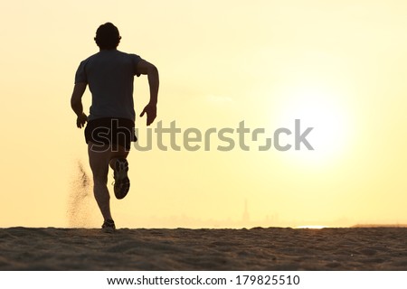 Back view silhouette of a runner man running on the beach at sunset with sun in the background