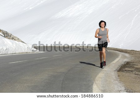 Runner happy woman running on a high snowy mountain road in winter