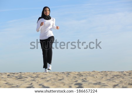 Front view of an arab saudi emirates woman running on the beach with the horizon in the background