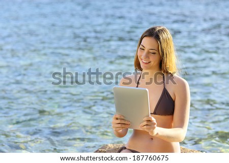Happy woman reading a tablet reader on the beach seaside with water in the background