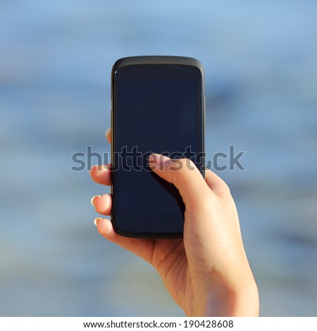 Woman hand holding and showing a blank smart phone screen on the beach with the sea in the background
