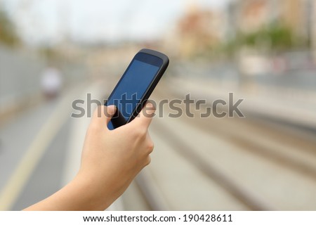 Woman hand holding a smart phone in a train station with the rails in the background